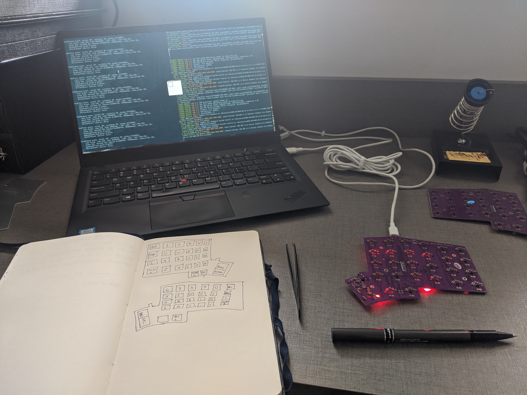 A laptop, a notebook with a drawing of the keyboard layout, and the PCB connected to the laptop